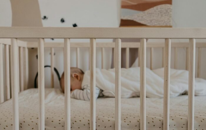 Recém-nascido dormindo de barriga para cima em um berço claro, sem objetos soltos